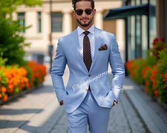 May include: A light blue suit with a white dress shirt and a patterned tie. The suit has a two-button closure and a pocket square. The image also includes sunglasses and a watch. The text "Theclothingstoreess" is visible.