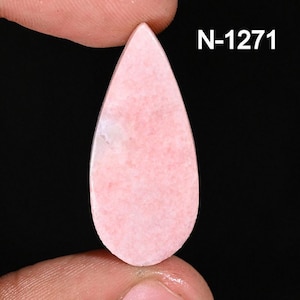 May include: A teardrop-shaped, polished gemstone in a soft pink hue. The stone has a smooth surface with subtle variations in color and a white inclusion. The text "N-1271" is visible in the upper right corner.