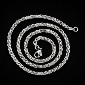 May include: A silver-toned wheat chain necklace featuring a polished metallic finish and a secure lobster claw clasp. The chain is coiled in a circular pattern, showcasing the intricate, braided link design that creates a uniform, textured appearance.
