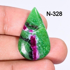 May include: A green and pink gemstone cabochon with a teardrop shape. The stone has a green base with pink and white veins running through it. The stone is labeled N-328.
