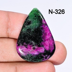 May include: A teardrop-shaped green, black, and pink gemstone cabochon. The stone has a unique pattern of swirls and streaks. N-326