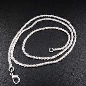 Può includere: Una collana a catena color argento caratterizzata da una texture intrecciata o simile a una corda continua. La collana include un piccolo anello di giunzione circolare a un'estremità e una chiusura a moschettone sicura all'altra.