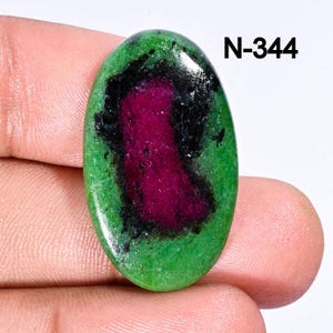 May include: Oval-shaped green gemstone with black and pink inclusions. The gemstone is approximately 2.5 cm in length. N-344