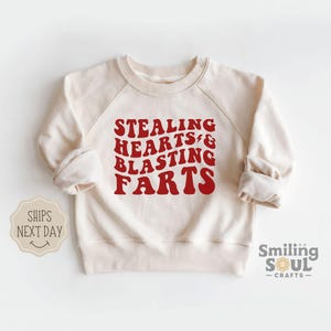 May include: A cream-colored sweatshirt with the text "STEALING HEARTS & BLASTING FARTS" in red.