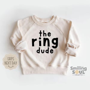 May include: A cream colored sweatshirt with black text that reads "the ring dude".