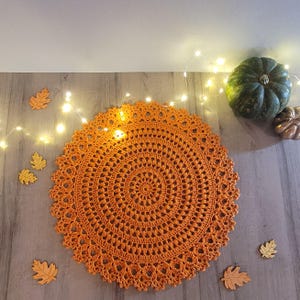 May include: Orange crochet doily with a delicate lace pattern. The doily is round and has a diameter of approximately 12 inches.