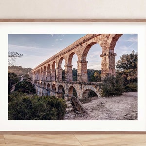 May include: A stone aqueduct with multiple arches, built into a hillside. The aqueduct is made of rough-hewn stone and is surrounded by trees and vegetation.