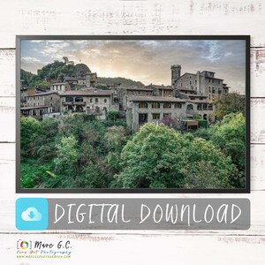 Peut inclure: Une photographie d'un petit village niché dans une vallée, entouré de luxuriants arbres verts. Le village est composé de bâtiments en pierre aux toits en terre cuite, et il y a un clocher au centre du village. Le ciel est d'un bleu doux avec quelques nuages.