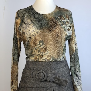 Könnte beinhalten: Ein langärmeliges Oberteil mit einem mehrfarbigen geometrischen Paisley-Muster in Braun, Beige und Olivgrün, kombiniert mit einem dunkelgrauen, strukturierten Minirock mit hoher Taille und passendem Gürtel mit runder Schnalle.