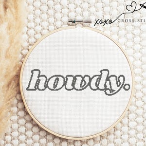 May include: A white embroidery hoop with the word "howdy" stitched in gray thread.