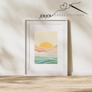 Puede incluir: Un patrón de punto de cruz enmarcado de una puesta de sol sobre un paisaje con montañas y agua. Los colores son un degradado de rosa, naranja, amarillo, azul y verde.
