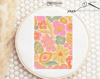 Könnte beinhalten: Kreuzstichmuster mit einem farbenfrohen abstrakten Blumendesign mit rosa, gelben, orangefarbenen und grünen Blumen. Das Muster ist in einem weißen Stickrahmen gerahmt.
