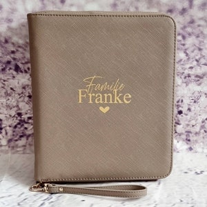Könnte beinhalten: Ein grauer Leder-Reißverschlussordner mit einer goldenen Aufschrift "Familie Franke" und einem kleinen goldenen Herz.