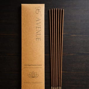May include: A brown package of hand-dipped bamboo incense with the text "95th Avenue". The package has a lotus flower graphic. The incense sticks are brown with gold tips, presented on a dark wooden surface.