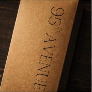 May include: A close-up shot of a brown cardboard box. The text "95th AVENUE" is printed vertically in black. The box has a simple, minimalist design.