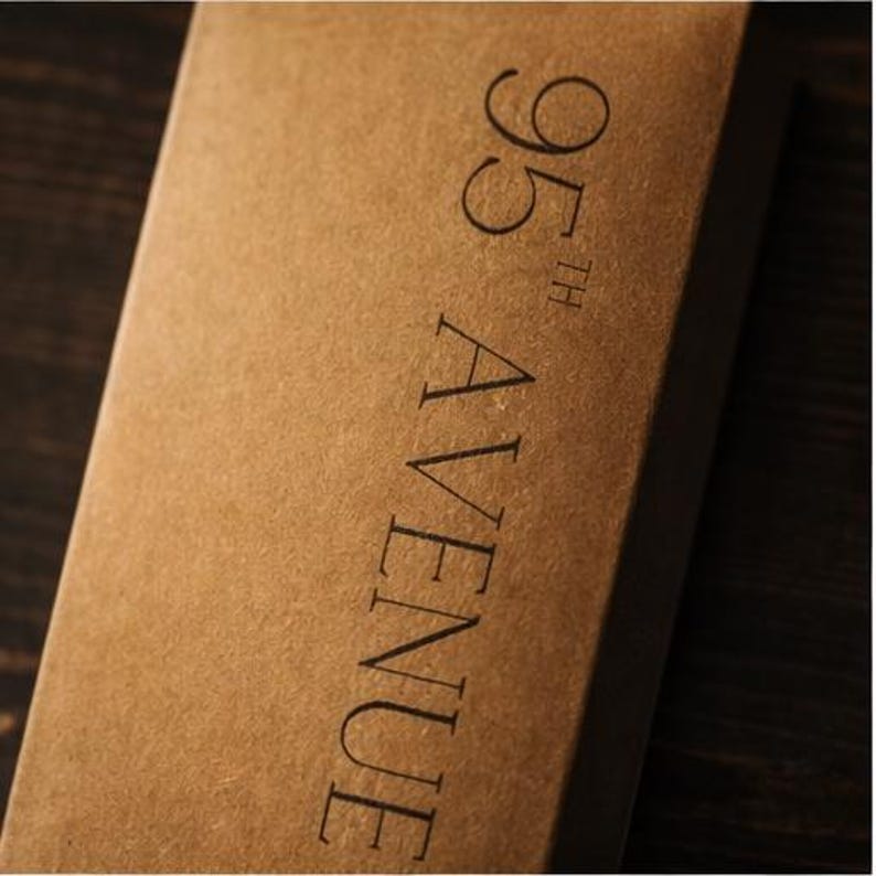 May include: A close-up shot of a brown cardboard box. The text "95th AVENUE" is printed vertically in black. The box has a simple, minimalist design.