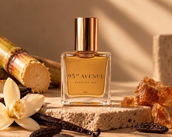 May include: A square glass bottle of 95th Avenue perfume oil with a gold cap. The label features the text 95th Avenue, Perfume Oil, and 10ml. The bottle is surrounded by a vanilla flower, vanilla beans, sugarcane, and amber-coloured resin chunks.