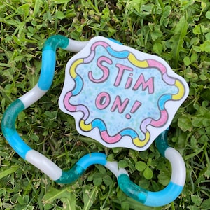 May include: A blue, white, and green fidget toy shaped like a snake with a sticker that says "Stim On!" in colorful letters on a white background.