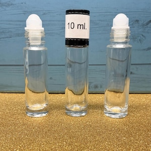 May include: Three clear glass roller bottles with white plastic roller balls. The center bottle features a black cap with a white label printed with the text 10 ml. The bottles are empty and cylindrical in shape, designed for holding liquid contents.