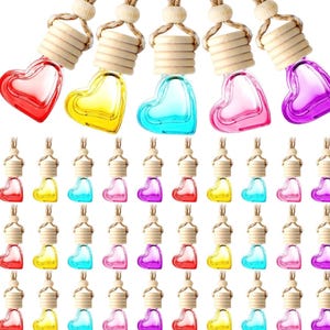May include: A collection of heart-shaped glass car air fresheners in various colors, including red, yellow, blue, pink, and purple. Each bottle has a wooden top and a hanging string. The background is white.