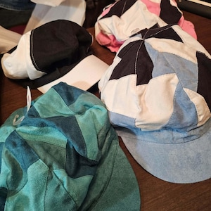 May include: A collection of four newsboy caps featuring various patchwork designs. One cap is teal and dark green, another is black and white, one is blue, black, and white, and the fourth is pink, black, and white. Each cap has a short brim.