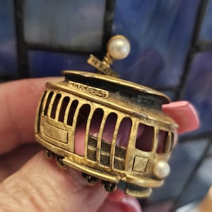 May include: Gold-toned metal trolley charm with a pearl on top and the words "MARKET ST" on the side.