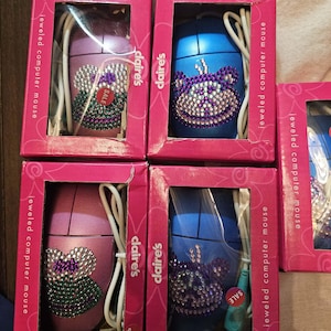 May include: Four Claire's brand jeweled computer mice in pink and blue boxes. Each mouse features a wired connection and a decorative rhinestone animal face design. The packaging includes the text jeweled computer mouse and Claire's.