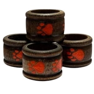 May include: Set of five wooden napkin rings. Each ring is dark brown with a red paw print design. The rings are cylindrical with a smooth, rounded top and bottom.