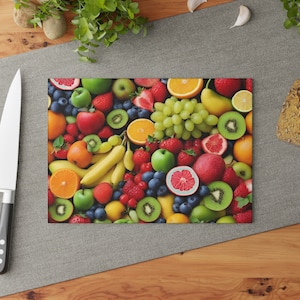 May include: A rectangular cutting board with a vibrant assortment of fresh fruits. The board is filled with strawberries, blueberries, kiwi, oranges, apples, grapes, and bananas. A stainless steel knife is on the left.
