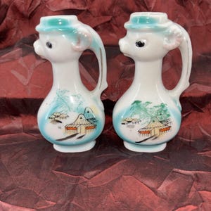 Könnte beinhalten: Eine weiße Keramiktasse mit schwarzem Henkel und dem Text "But First, Coffee" in fetter, schwarzer Schrift. Die Tasse steht auf einer weißen Oberfläche und zeigt ihr schlichtes Design.