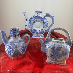 Puede incluir: Tres teteras de porcelana azul y blanca con intrincados diseños florales. Las teteras están sobre un fondo de tela roja.