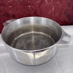 Op de afbeelding: Een rustiek houten bord met de handgeschreven tekst "Welcome". Het bord is wit geschilderd met een verweerde afwerking en heeft een decoratief bloemelement. De achtergrond is een vage afbeelding van een houten oppervlak.