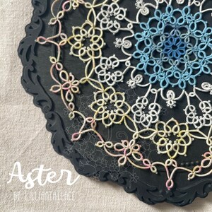 Puede incluir: Un delicado encaje circular con un degradado de colores que va del rosa al amarillo, al blanco y al azul. El encaje se muestra sobre un fondo negro con un borde decorativo. El texto "Aster by Lilliantatlace" es visible debajo del encaje.