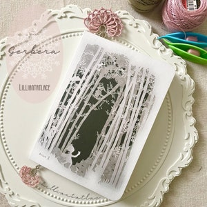 May include: A rectangular notebook featuring a white paper-cut style forest scene with tall trees and a small figure on a dark background. The cover includes the text Gerbera and Lilliantatlace. Two pink lace tatting bookmarks are attached.