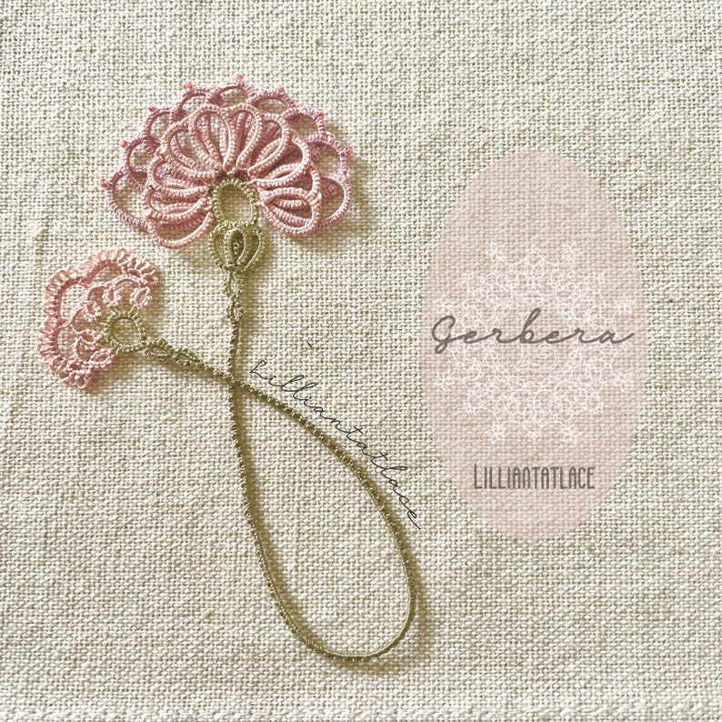 May include: A delicate tatting lace bookmark featuring two pink floral motifs connected by a thin, light brown thread stem. The design includes the text Gerbera and LILLIANTATLACE printed on the fabric background near the lace ornament.