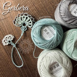 May include: Four balls of Scheepjes Candy Floss 100% organic mercerised cotton yarn in shades of grey, light blue, and pale green, alongside a delicate, hand-crocheted lace motif featuring a fan-like design and a thin, looped thread tail.
