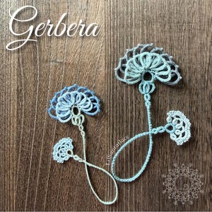 May include: Two delicate tatting lace bookmarks in shades of light blue and white. Each bookmark features a fan-shaped floral motif at the top, a long thin stem, and a smaller decorative fan-shaped element at the bottom end of the thread loop.