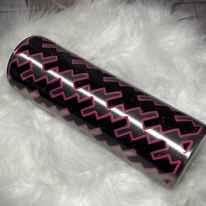 May include: A black and silver stainless steel tumbler with a pink geometric pattern. The tumbler has a black lid and a silver base.