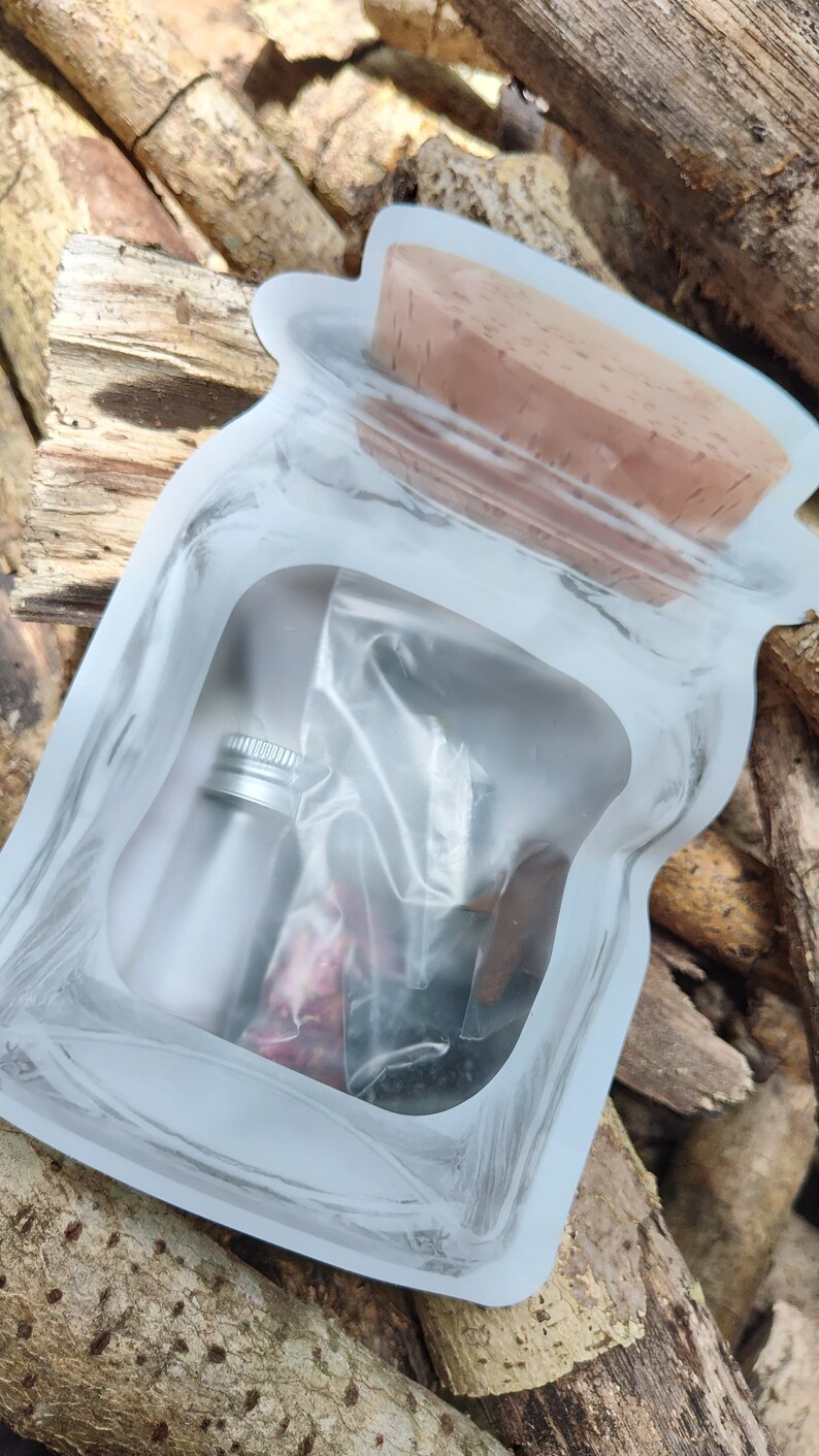 May include: A clear plastic pouch with a brown cork lid. Inside the pouch are a small silver bottle and a clear plastic bag with dried herbs and flowers.