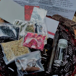May include: A protection spell bottle kit with instructions on a white piece of paper. The kit includes a variety of herbs, crystals, a candle, and an anointing oil. The kit is on a red and black plate.