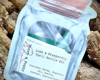 May include: A clear plastic bag with a corked glass bottle inside. The bag has a label that reads "Luck & Prosperity Spell Bottle Kit" and includes a list of ingredients: herbs, crystals, oil, bottle, incense, and instructions. The bag is sitting on a pile of tree branches.