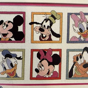 Può includere: Sampler a punto croce con sei personaggi Disney: Topolino, Pippo, Paperina, Paperino, Minnie e Pluto. Ogni personaggio è incorniciato in un colore diverso, su sfondo bianco e racchiuso in un bordo rosa.