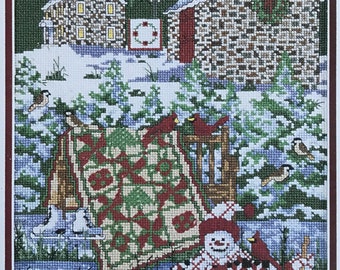 Puede incluir: Una escena de invierno en punto de cruz representa un paisaje nevado con dos edificios de piedra, una colcha y un muñeco de nieve. La colcha presenta un patrón rojo y verde. Cardenales y gorriones están dispersos por la escena. Un muñeco de nieve con un abrigo estampado en rojo y blanco sostiene una escoba.