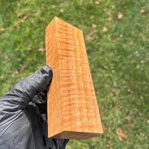 May include: A block of wood with a reddish-brown color and a unique grain pattern. The wood has a smooth, polished finish.