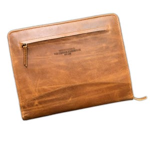May include: A tan leather document portfolio featuring a horizontal zippered pocket on the front. The leather has a distressed finish and is embossed with the text PREMIUM LEATHER CO. THE LEATHER WAREHOUSE EST. 2015 near the top centre.