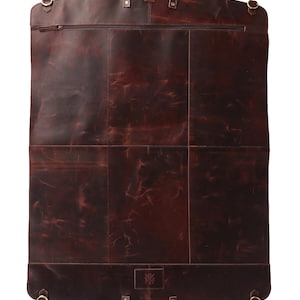 May include: A dark brown leather garment bag with a top handle and a bottom handle. The bag has a zipper closure and several metal accents. The leather has a distressed appearance.