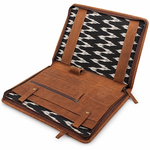 May include: A brown leather portfolio case with a zip closure, featuring an interior lined with a black and white zigzag ikat pattern. The interior includes multiple pockets, card slots, a pen loop, and two leather straps with brass snaps.