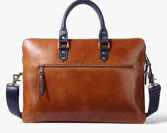 Può includere: Una valigetta in pelle marrone con manico e tracolla blu navy. La valigetta ha una tasca frontale con cerniera e chiusura a fibbia in ottone.