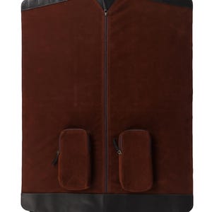 May include: A brown garment bag with black leather trim and a handle. The bag has a full-length zipper and two small pockets. The bag is designed to protect clothing during travel.