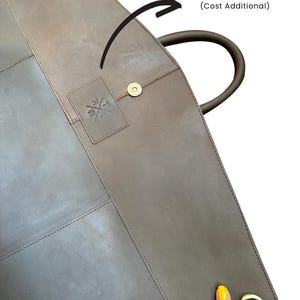 May include: A brown leather garment bag with a handle and a brass-colored clasp. The bag has a stitched design and a small embossed logo. The text "GET YOUR COMPANY / BRAND LOGO HERE" is also visible.